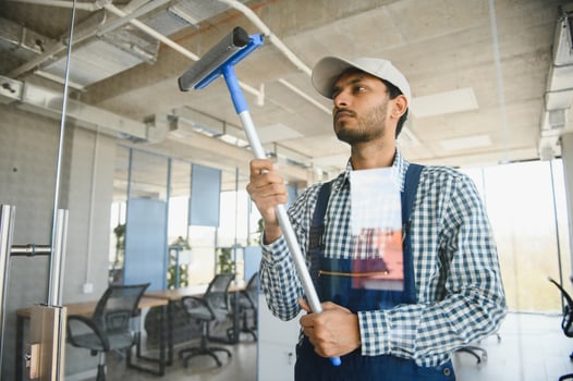 Male janitor cleaning window in office photo