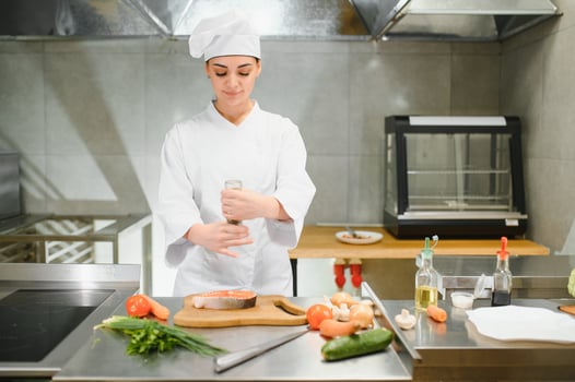 young beautiful female chef cooks salmon in restaurant kitchen photo