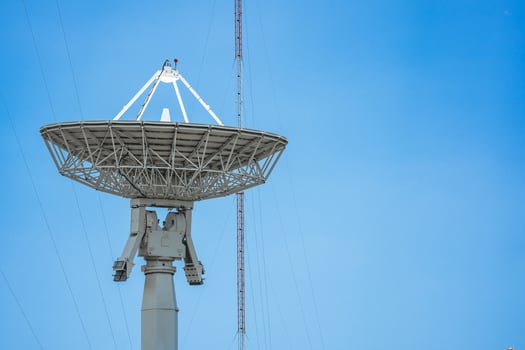 parabolic antenna satellite dish located in front of telecommunication tower with a clear blue sky in the background. photo