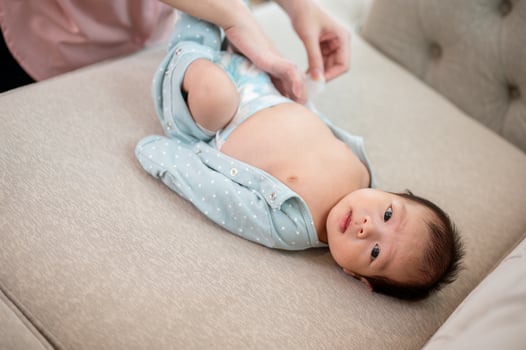 An adorable Asian newborn baby is being dressed or having pajamas put on by his mom on the sofa. photo