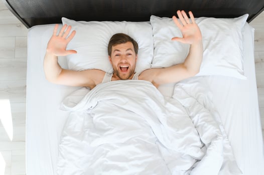 Cheerful Man Waking Up Lying In Cozy Bed At Home On Weekend Morning. Healthy Sleep Concept photo