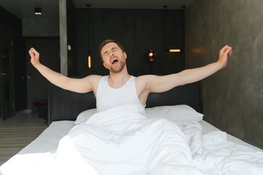 Young man sleeping waking up and stretching in his bed photo