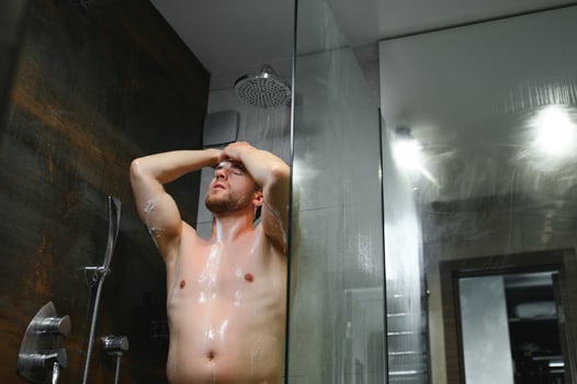Handsome Young Man Taking A Shower Standing Under Falling Water Drops Washing Naked Body And Head In Modern Bathroom At Home. Male Model photo