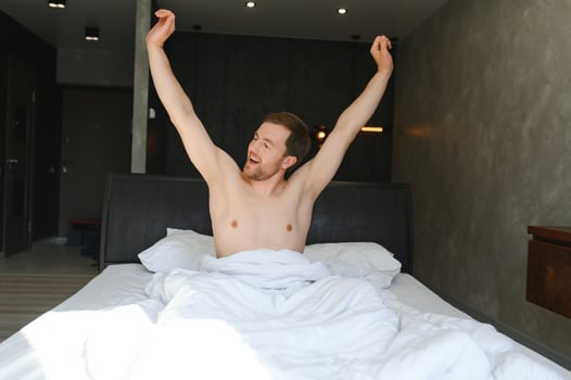 Young man sleeping waking up and stretching in his bed photo
