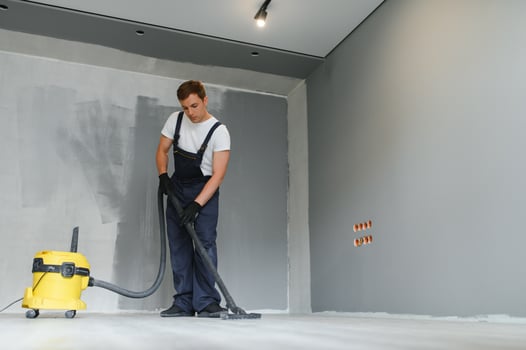 A worker using a vacuum cleaner removes construction debris. A worker is cleaning industrial premises. apartment after repair using polysos photo