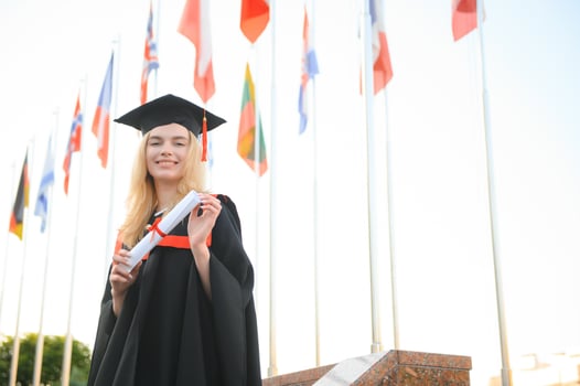 Happy university graduate girl. The girl is standing near the university against the background of the flags of different countries. The concept of international education. photo