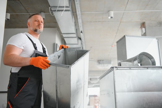 Man repairman. Master near ventilation pipes. Installation of ventilation for buildings. Man repairman with back to camera. Metal ventilation pipes. photo