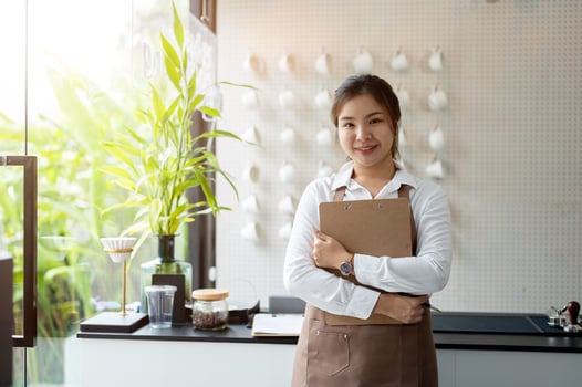 A charming Asian female barista in a brown apron is standing in a minimal white coffee shop. photo