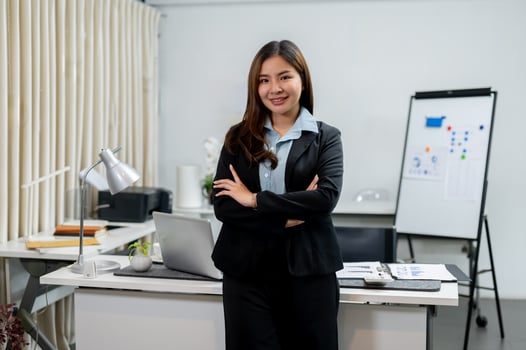A confident Asian businesswoman in a business suit is standing with her arms crossed in the office. photo