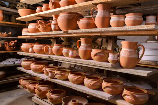 Freshly made clay mugs, pots and bowls drying up on wooden shelves in pottery workshop. Handmade ceramics manufacture. Different clay pots in workshop. photo