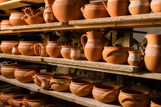 Freshly made clay mugs, pots and bowls drying up on wooden shelves in pottery workshop. Handmade ceramics manufacture. Different clay pots in workshop. photo