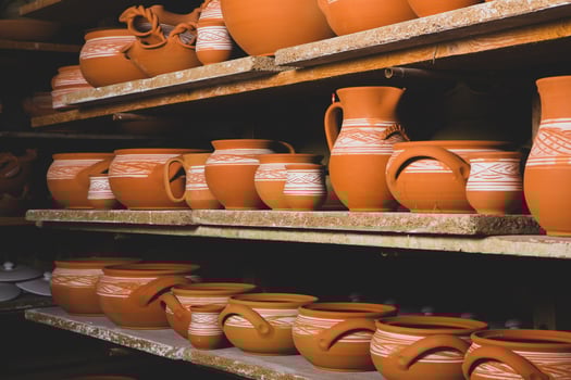 Freshly made clay mugs, pots and bowls drying up on wooden shelves in pottery workshop. Handmade ceramics manufacture. Different clay pots in workshop. photo