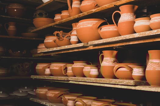 Freshly made clay mugs, pots and bowls drying up on wooden shelves in pottery workshop. Handmade ceramics manufacture. Different clay pots in workshop. photo