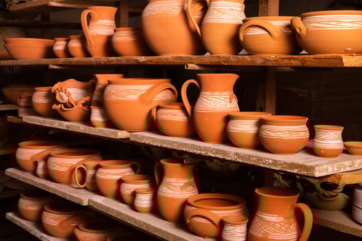 Freshly made clay mugs, pots and bowls drying up on wooden shelves in pottery workshop. Handmade ceramics manufacture. Different clay pots in workshop. photo