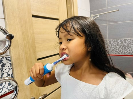 A happy little Asian girl brushes her teeth in the bathroom. Morning routine. Hygiene. Healthy lifestyle photo