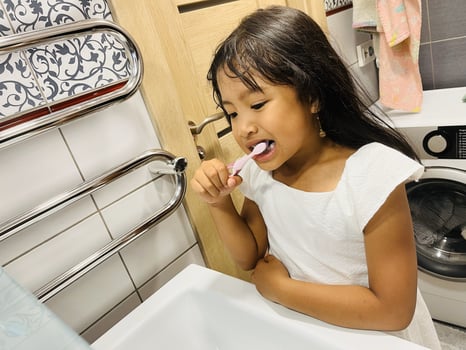 A happy little Asian girl brushes her teeth in the bathroom. Morning routine. Hygiene. Healthy lifestyle photo