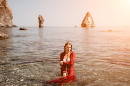 Woman travel sea. Happy tourist in red dress enjoy taking picture outdoors for memories. Woman traveler posing in sea beach, surrounded by volcanic mountains, sharing travel adventure journey photo