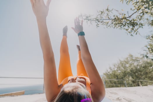 Fitness woman sea. Happy middle aged woman in orange sportswear exercises morning outdoors on yoga mat with laptop in park over ocean beach. Female fitness pilates yoga routine. Healthy lifestyle. photo