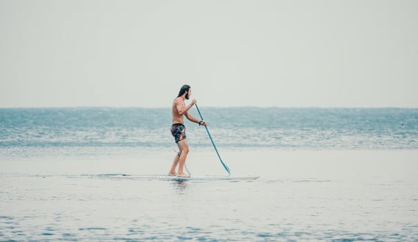 Sea man sup. Asian athlete man swimming in sea and paddleboarding at summer sunset. Healthy strong male enjoy outdoor active lifestyle and water sports on holiday vacation. photo