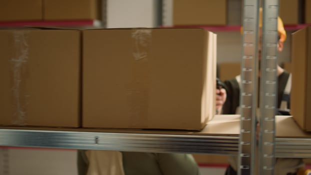 Focused warehouse employee and colleague scanning cardboard boxes on cabinet shelves, updating storage room merchandise labels info before sending parcels to be dispatched photo