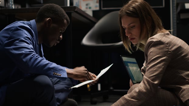 Multiethnic private investigators pursuing the truth in crime case, gathering evidence in incident room. Black policeman and caucasian detective sitting on floor surrounded by clues, files and laptop. photo