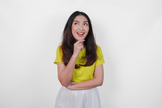 Smiling young Asian woman in a yellow shirt and white skirt is looking up, thinking about an idea or feeling excited about something, isolated by white background. photo