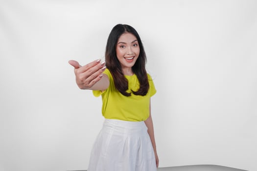 Joyful Asian woman in a yellow shirt and white skirt is smiling and inviting people to come, isolated by white background. photo