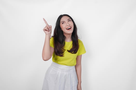 Happy young Asian woman wearing yellow shirt and white skirt presenting the copy space upside, isolated by white background. photo