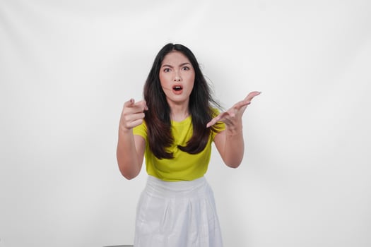 Surprised woman in a yellow shirt pointing to the front with mad expression on her face, isolated by white background. photo