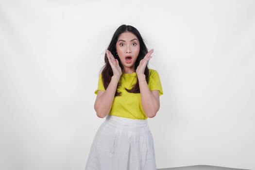 A beautiful woman in a yellow shirt and white skirt is looking shocked isolated by white background. photo