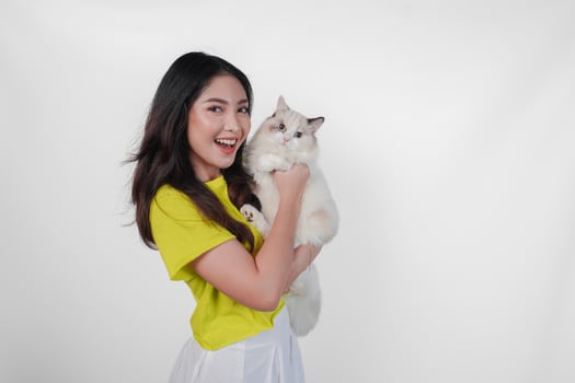 Smiling young Asian woman in yellow shirt is holding a white ragdoll cat over isolated white background. photo
