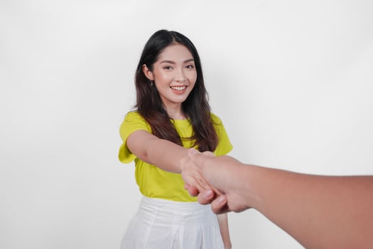 Cheerful young Asian woman in a yellow shirt is giving a handshake to a man. The woman is smiling and the man is reaching out to shake her hand. Concept of warmth and friendliness. photo