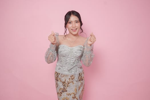 Cute Indonesian woman wearing modern kebaya dress and feeling excited, isolated by a pink background. photo