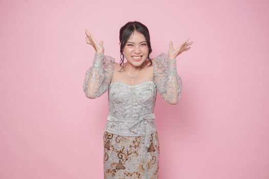 Irritated young Indonesian woman wearing modern kebaya dress expressing annoyed, mad, frustrated feelings, isolated over pink background. photo