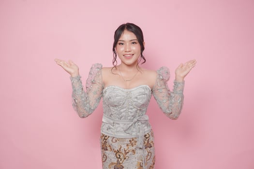 Beatiful Asian woman wearing modern kebaya dress presenting copy space on her left and right side, isolated by pink background. photo