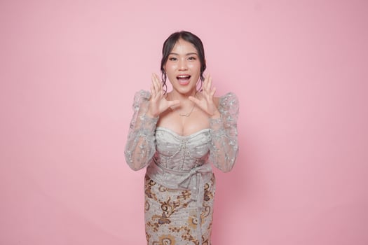 Cheerful Asian woman wearing modern kebaya dress feeling surprised and shouting wow, isolated by pink background. photo