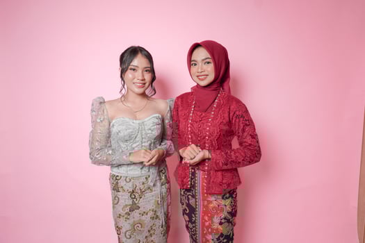 Two young Asian women wearing modern kebaya dress standing and smiling at camera over isolated pink background. photo