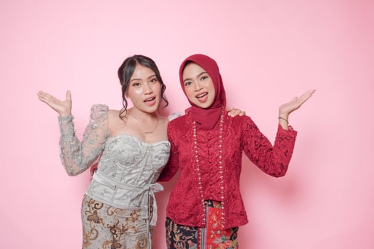 Two cute Asian young woman wearing modern kebaya presenting copy space upwards, isolated over pink background. photo