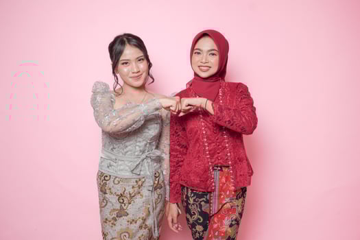 Smiling Asian young women wearing modern kebaya showing fist bump sign, isolated over pink background. photo