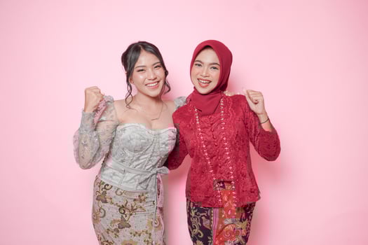 Two excited Asian women wearing modern kebaya dress with a happy successful expression, isolated by pink background. photo