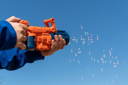 A boy holds a bubble gun and blows bubbles into the clear blue sky photo