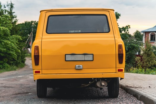 A yellow van is parked on a paved street with a house in the background photo