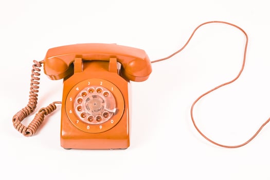 Vintage orange rotary dial telephone with a coiled cord, on a white background, studio shot. photo