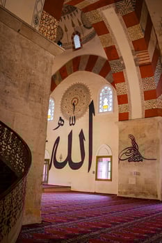 Interior of a mosque with large Arabic calligraphy on the walls and pillars with people are seen walking and praying on a red patterned carpet, in Edirne, Turkey. photo