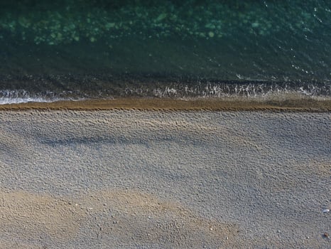 Aerial view from above on azure sea and pebbles beach. Small waves on cristal clear water surface in motion blur. Nature summer ocean sea beach background. Nobody. Holiday, vacation and travel concept photo
