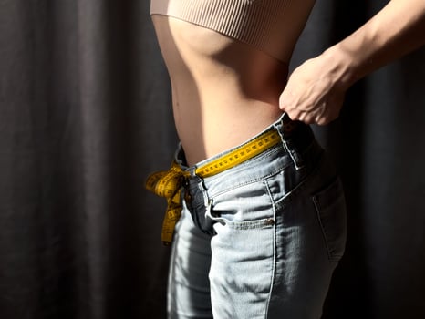 Close up of the naked torso of faceless woman in jeans with yellow measuring tape instead of belt on neutral background. Weight loss, fitness and body measurement concept. Lifestyle photo. photo