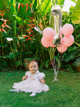 Birthday of cute baby girl with air balloons in summer garden. Happy child in dress. photo