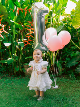 Birthday of baby girl with air balloons in outdoor garden. Happy child in dress. photo
