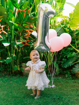 One year birthday of baby girl with air balloons in garden. Charming little child in dress. photo