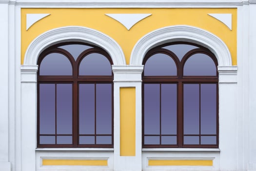 Close up view on a facade of white yellow ancient building with two arched windows as texture photo